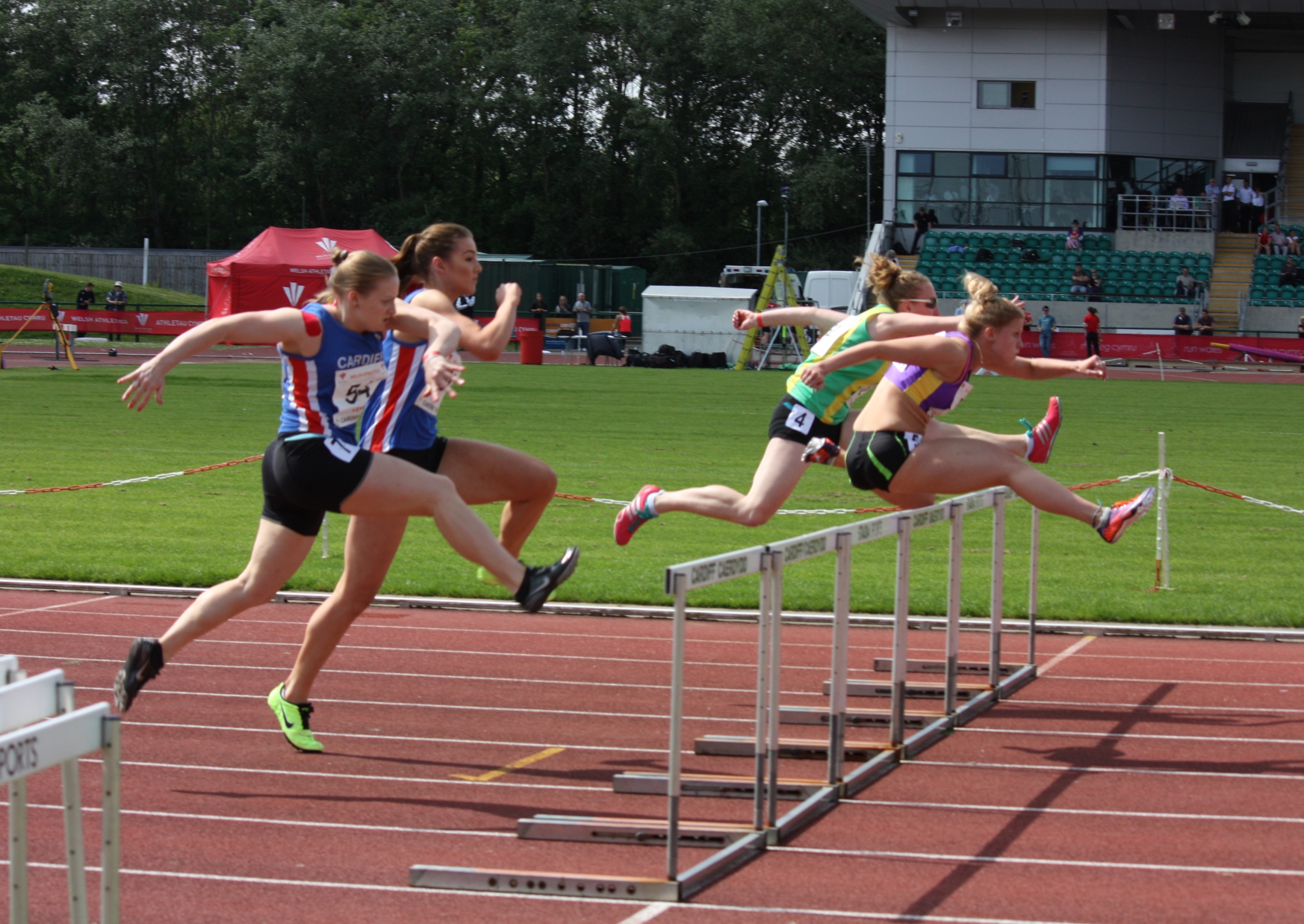 Four women jumping over running hurdles