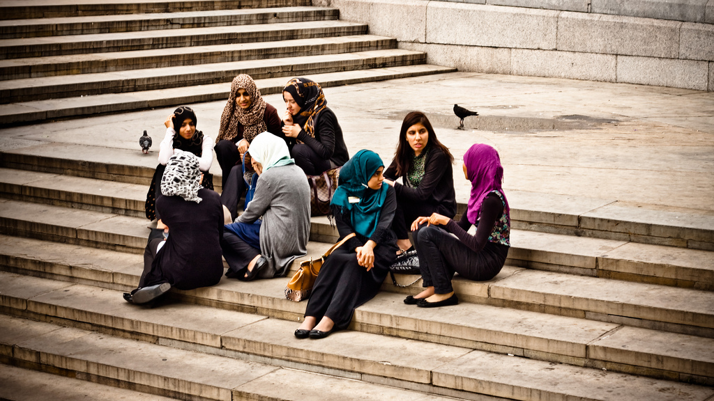 A group of women of colour, some wearing headscarves, sitting on stone steps