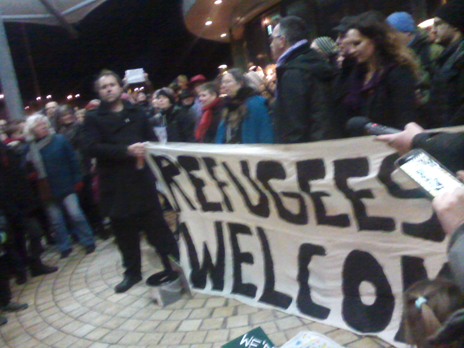 Group of individuals holding a banner Refugees Welcome