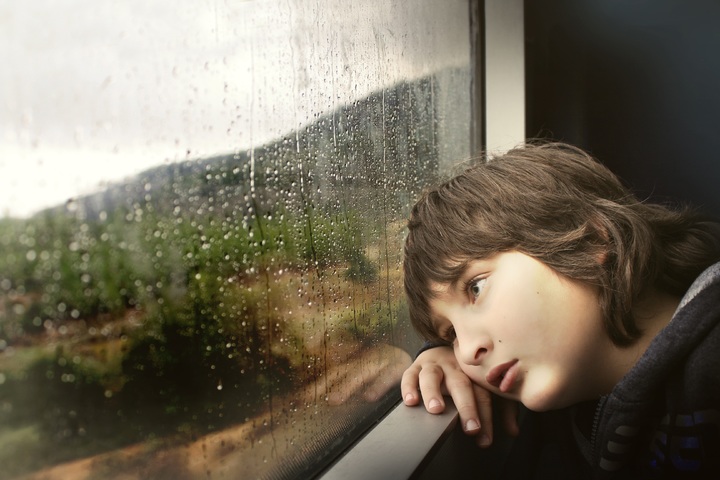 Child looking out of window at rainy landscape
