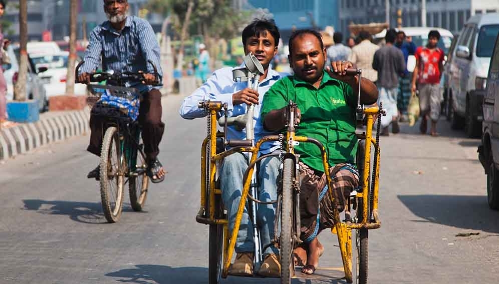 Picture of two men driving a hand-powered two-person bikeerson bike down a road in India, one with crutches