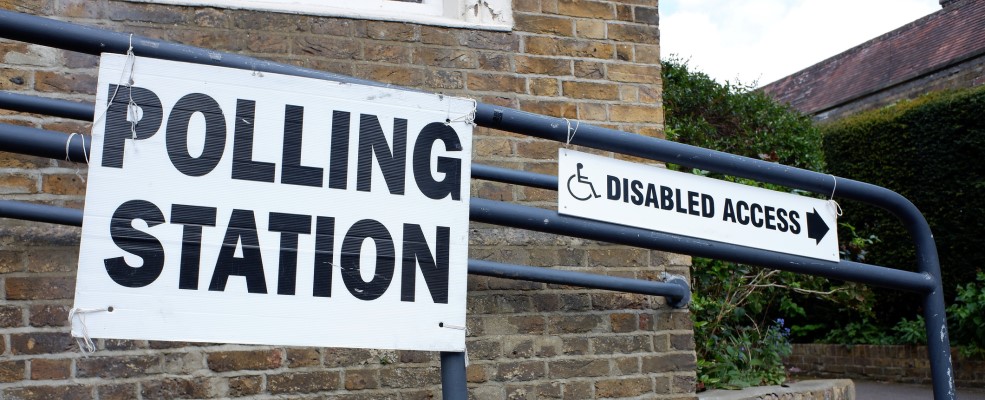 Handrail next to building with signs saying 'POLLING STATION' and 'DISABLED ACCESS'.