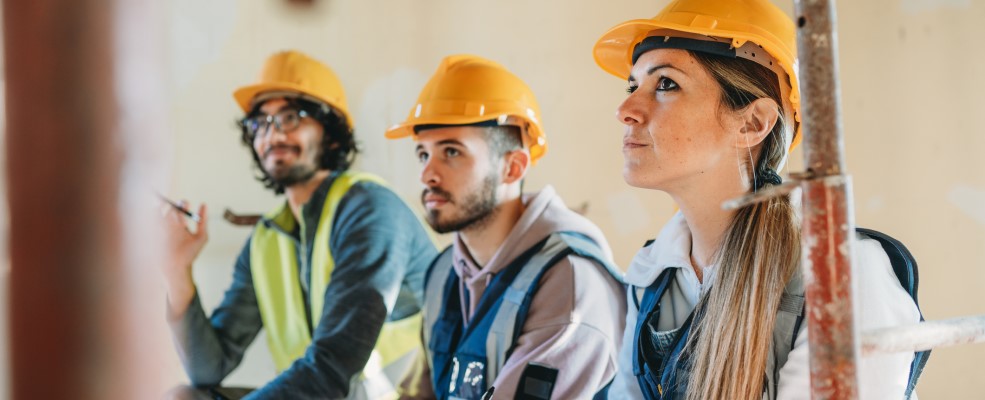 Three people are listening to their foreman on a construction site.