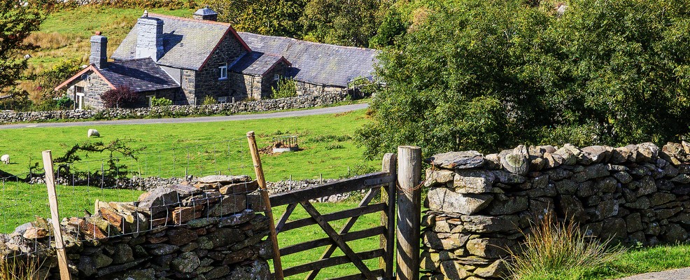 Welsh countryside with house in the background and stone wall with gate in the foreground.