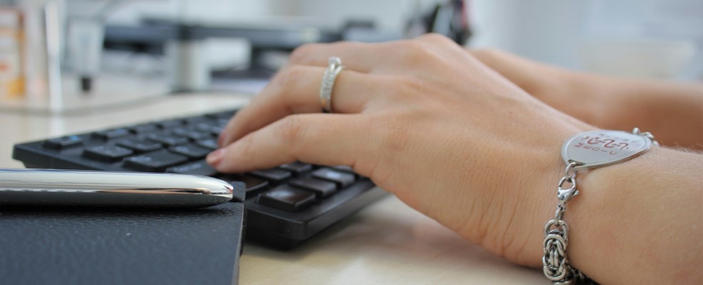 Close-up of a person's wrists and hands while working on a computer keyboard. They are wearing a medical bracelet.